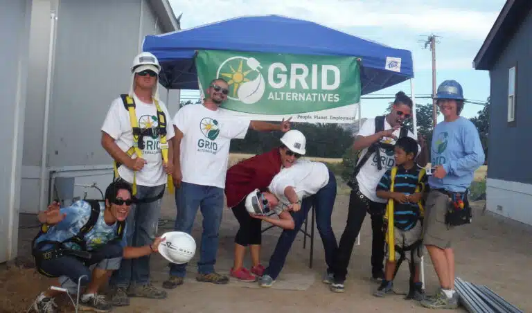Group of GRID Alternatives volunteers and staff posing under blue tent at outdoor event