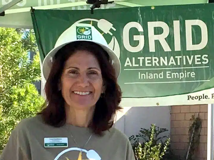 Woman smiling at GRID Alternatives Inland Empire booth wearing hard hat and volunteer shirt