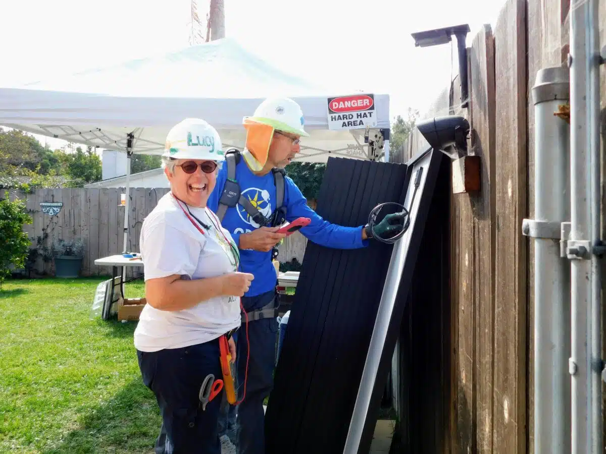 Two workers in hard hats and safety gear inspect industrial equipment in a backyard, with a "Danger Hard Hat Area" sign visible