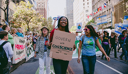 Protesters marching with signs including "Govern by Conscience" at a crowded city street demonstration