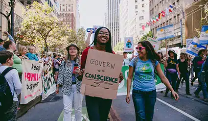 Protesters marching with signs including "Govern by Conscience" at a crowded city street demonstration
