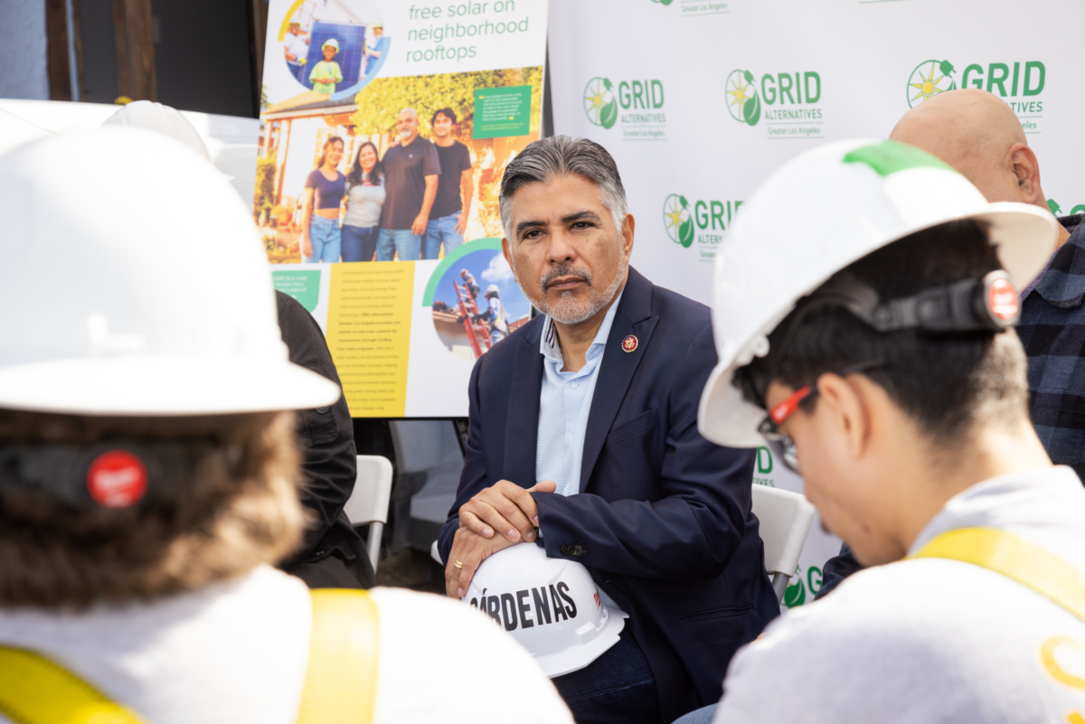 Man in navy blazer speaking with workers wearing hard hats at GRID Alternatives event