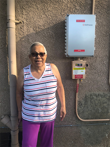 Woman in striped tank top standing next to Enphase solar inverter on gray wall