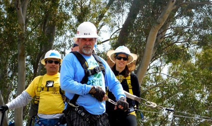 Three people in safety gear on a high ropes course among trees