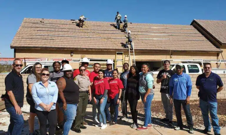 Group of volunteers posing in front of a house undergoing roof repair work
