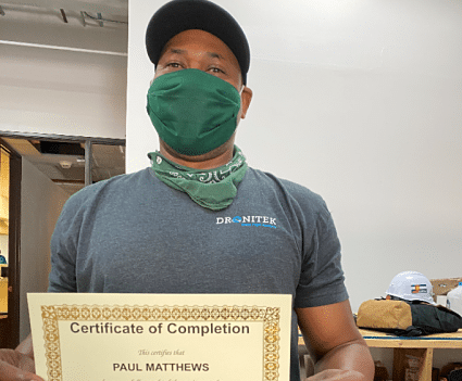 Paul Matthews holding a Certificate of Completion while wearing a green mask and black cap