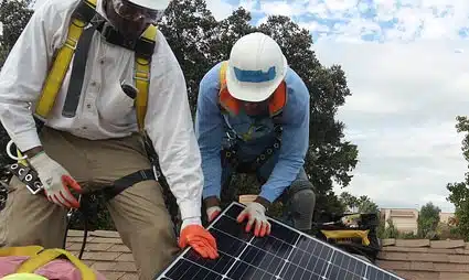 Two workers in safety gear installing a solar panel on a rooftop