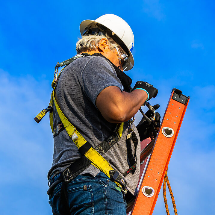 Construction worker on ladder holding level against blue sky
