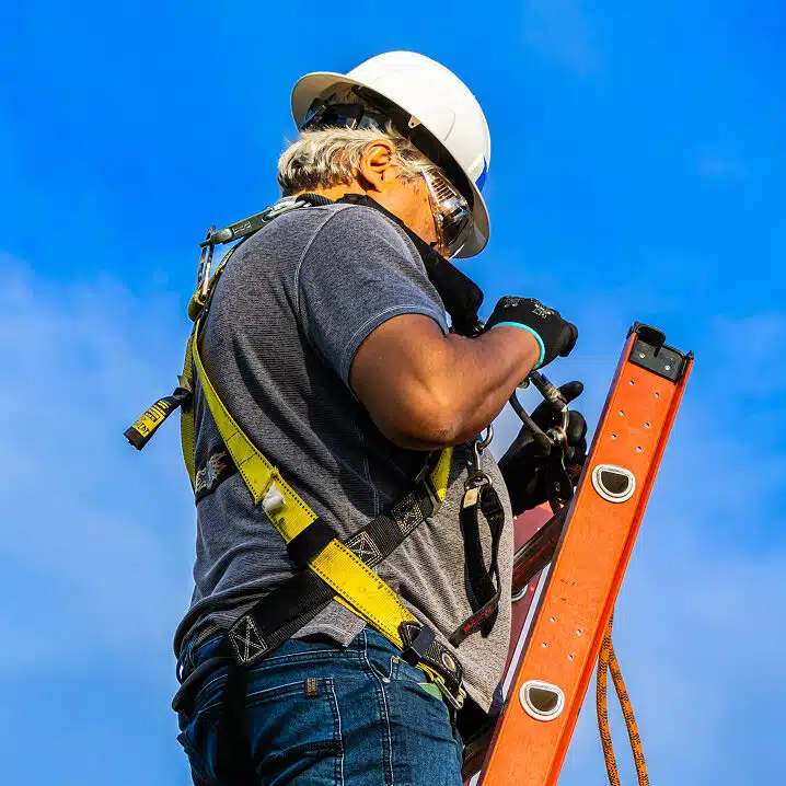 Construction worker on ladder holding level against blue sky