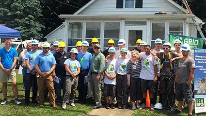 Group of volunteers in hard hats standing in front of a house during a community building project