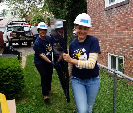 Two volunteers carry a solar panel
