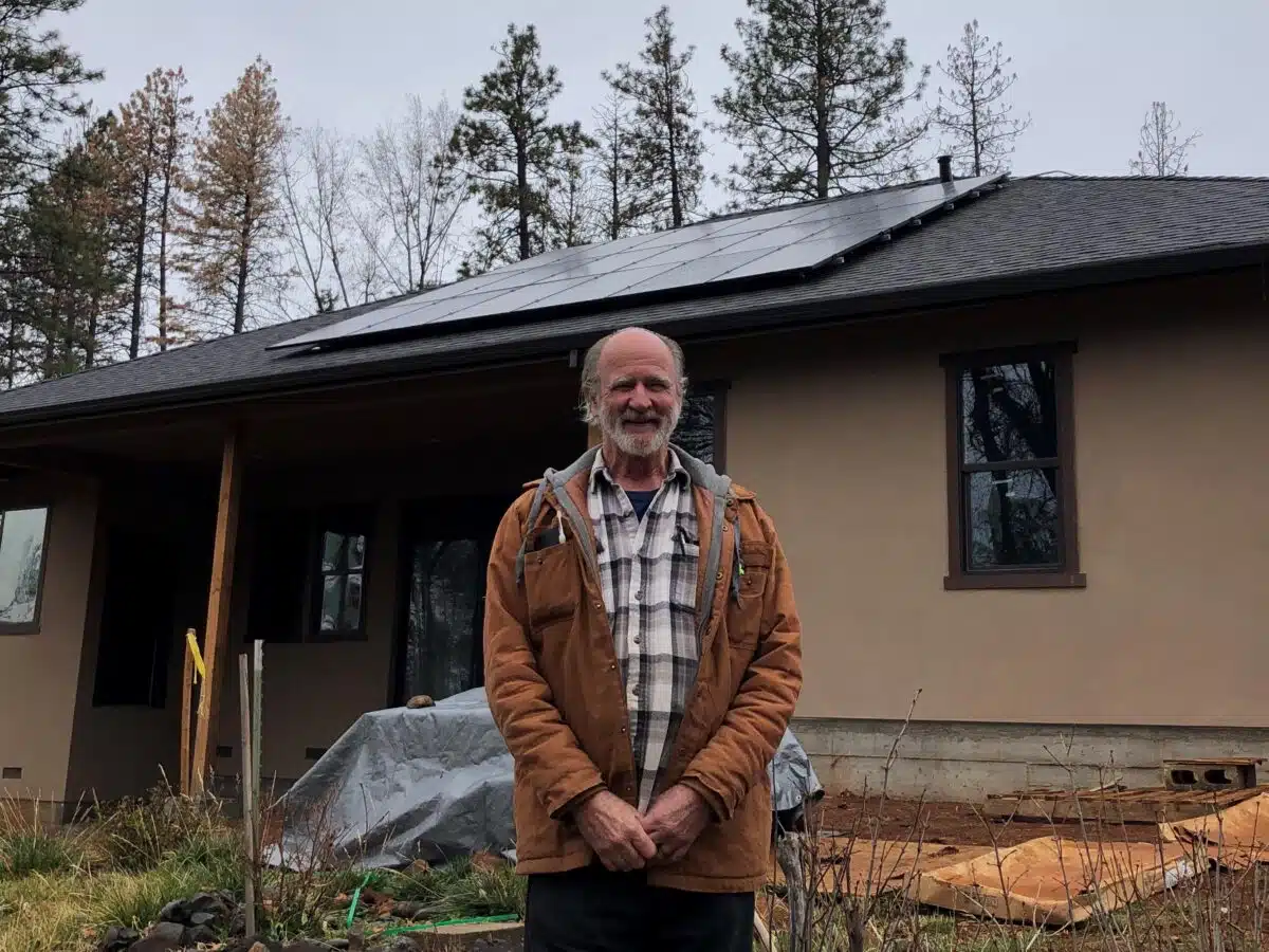 Man standing in front of modern home with solar panels and forest backdrop