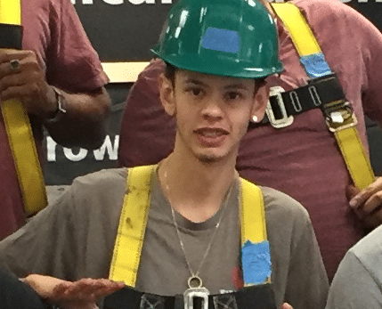 Young man wearing green hard hat and yellow safety vest at construction or trade event