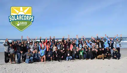SolarCorps Grid team group photo on beach with logo and raised arms celebrating