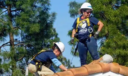 Two workers in safety gear installing large pipes on a roof structure