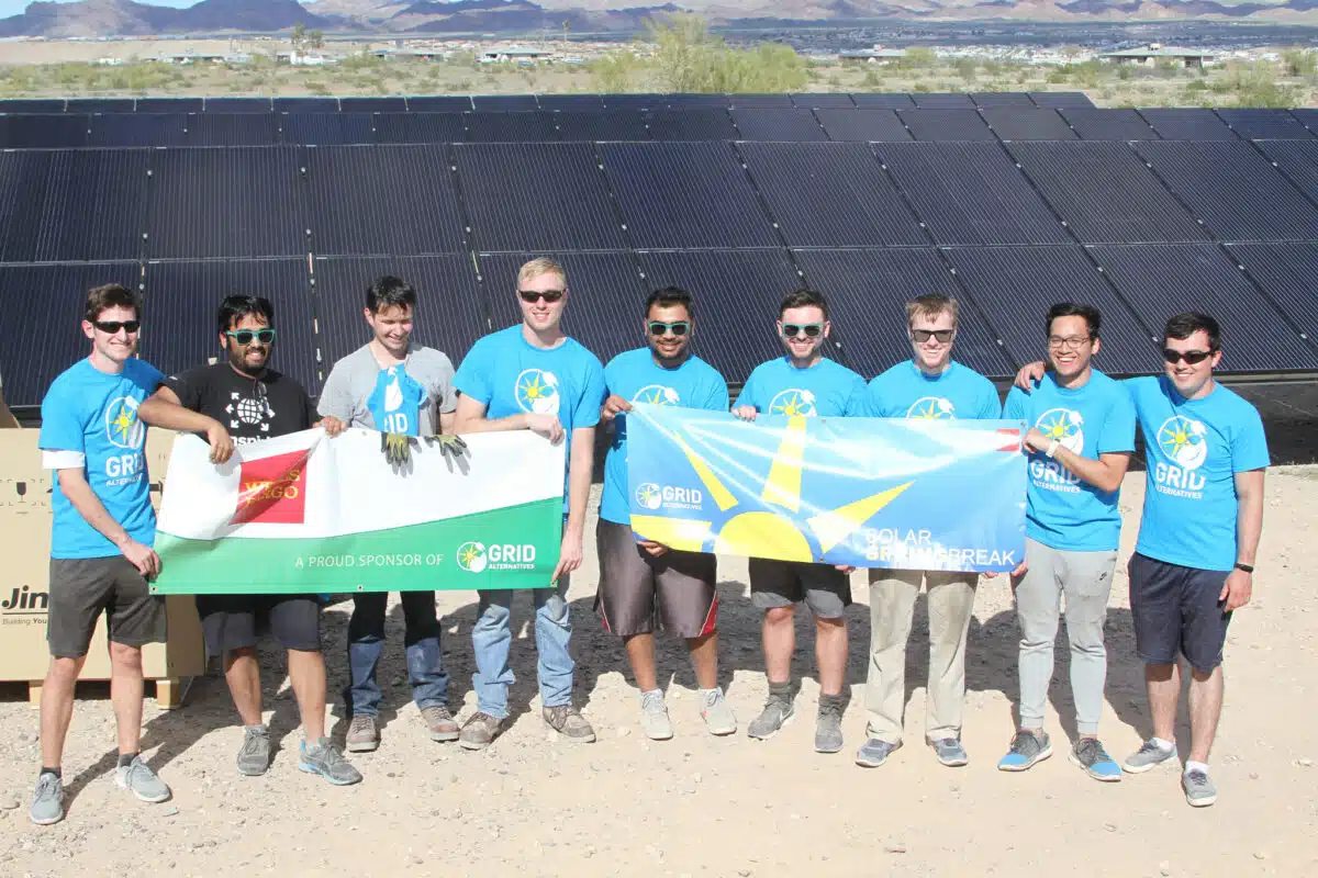 Team in blue GRID shirts holding solar and flags at solar panel installation site