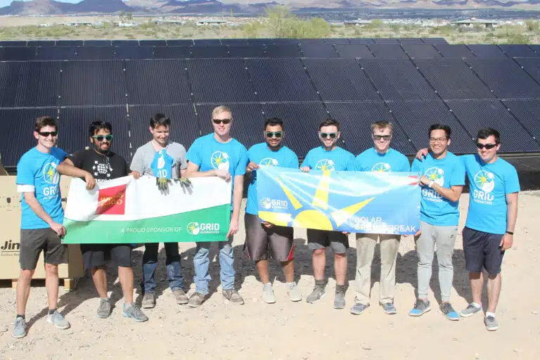 Team in blue GRID shirts holding solar and flags at solar panel installation site