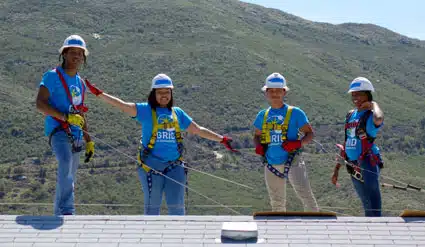 Four students pose on a rooftop while installing solar.