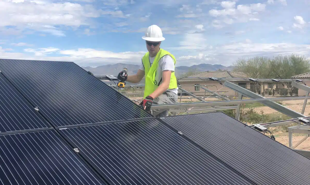 Construction worker installing metal roofing panels on residential building with mountains in background