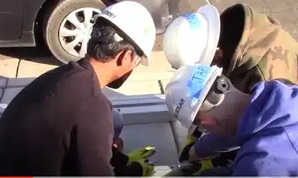 Two construction workers in safety helmets and vests examining building materials or plans on a vehicle