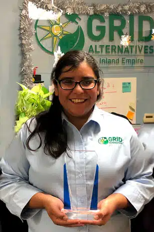 Woman holding award in front of GRID Alternatives Inland Empire office sign