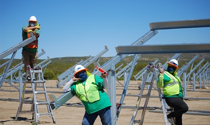 Construction workers in safety gear installing solar panel equipment at a renewable energy site