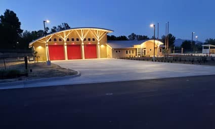Soboba fire station exterior at dusk with illuminated yellow wooden roof and red garage doors