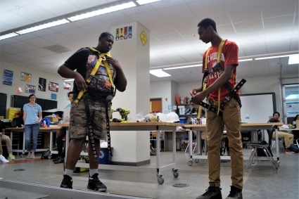 Two high school students demonstrate how to correctly wear a safety harness during a class presentation.