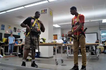 Two high school students demonstrate how to correctly wear a safety harness during a class presentation.