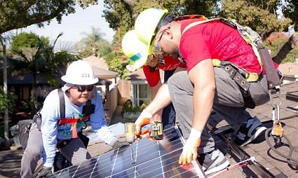 Two workers installing solar panels on a residential rooftop during a community solar installation event