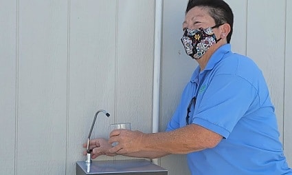 Man in blue shirt wearing mask washing hands at sink