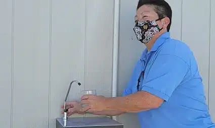 Man in blue shirt wearing mask washing hands at sink