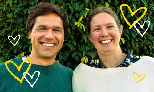 Two smiling people against green foliage background with yellow and white heart decorations