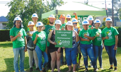 Group of volunteers in green GRID shirts and hard hats holding a sign at an outdoor event
