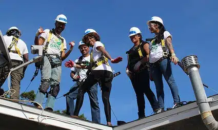 Group of workers in hard hats and safety vests standing on a metal roof structure against blue sky