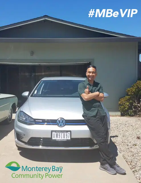 Man posing with white Volkswagen e-Golf electric car, #MBeVIP hashtag, Monterey Bay Community Power logo