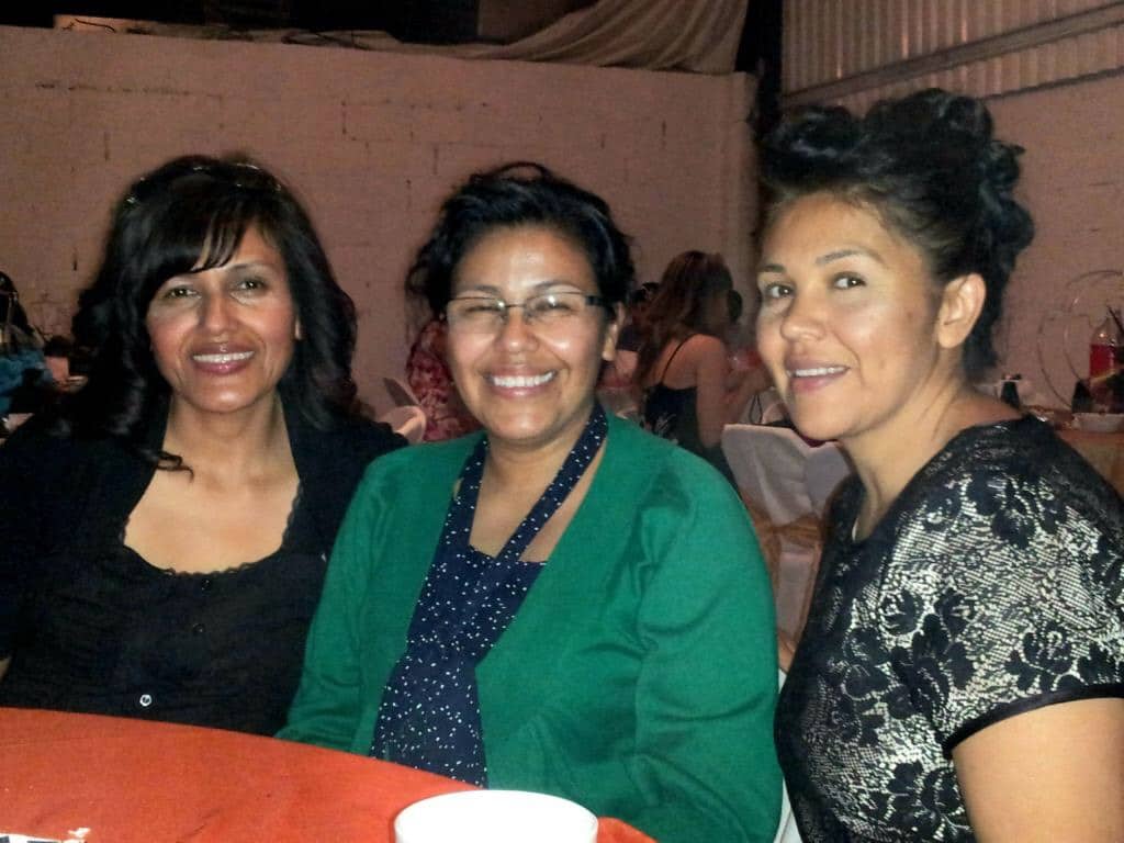 Three women smiling at an indoor event, seated at a table with a red tablecloth