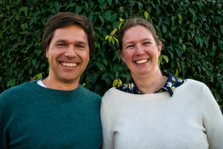 Two smiling people posing together in front of green foliage