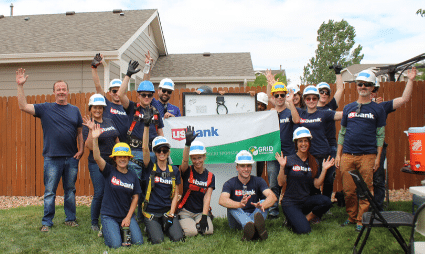 Group of volunteers in hard hats holding a U.S. Bank banner at a community build event