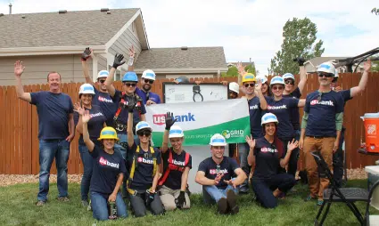 Group of volunteers in hard hats holding a U.S. Bank banner at a community build event