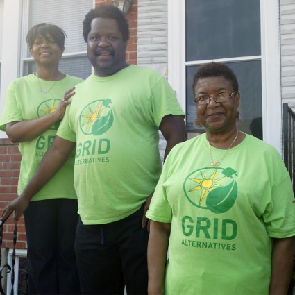 Three people wearing bright green GRID Alternatives t-shirts stand together outdoors