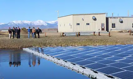 Floating solar panels on water with modern building and snow-capped mountains in background