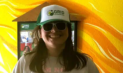 Person wearing GRID cap and sunglasses smiling in front of yellow abstract background
