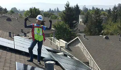 Worker in safety gear celebrating on residential roofing project with mountains in background