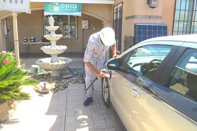 Man charging electric vehicle outside Grid Alternatives storefront