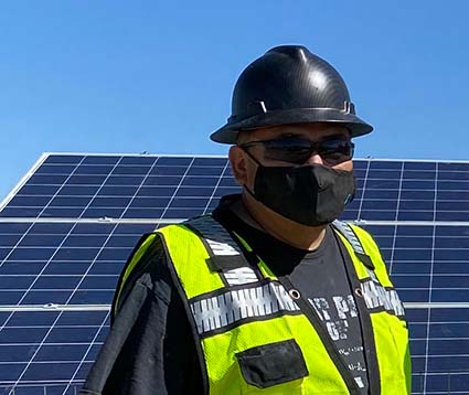 Worker in safety gear standing in front of solar panels