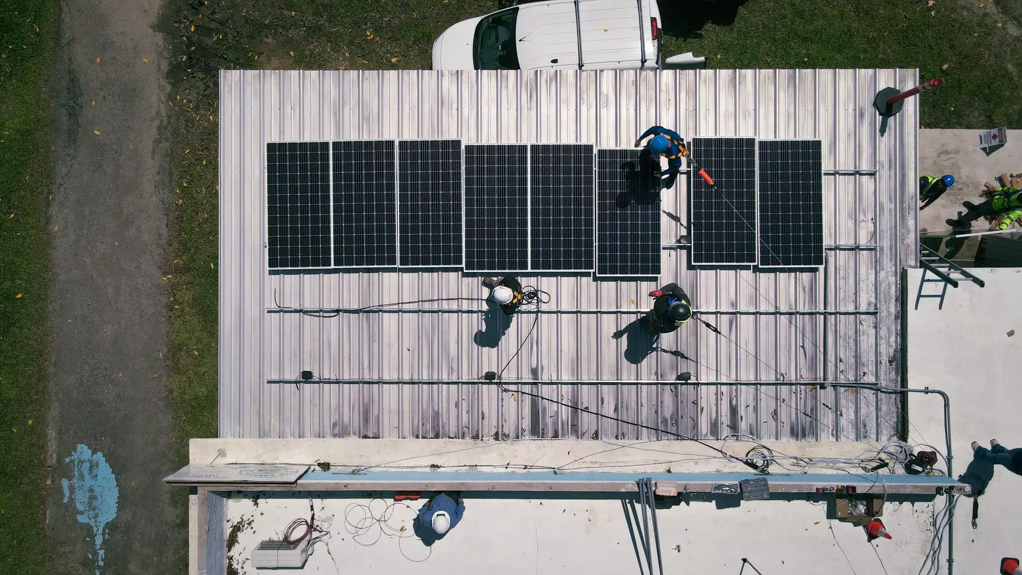 An overhead view of installers fitting solar panels to the roof of a single-storey building.