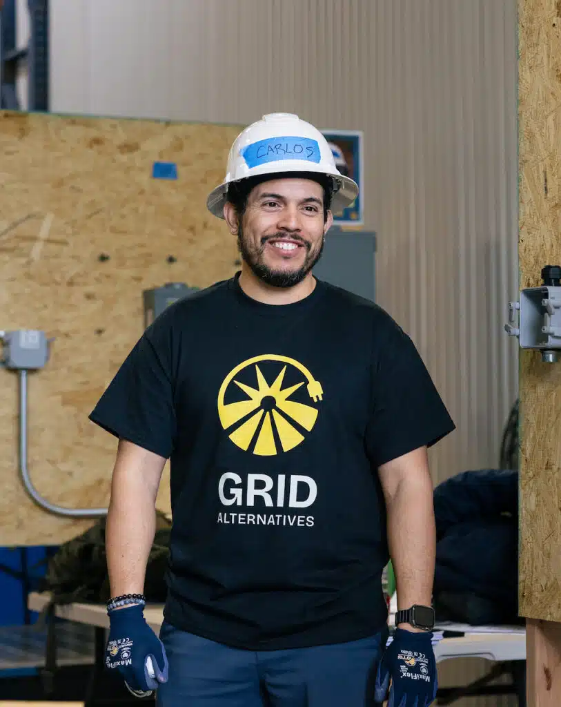 Two GRID staff members in branded T-shirts talk in a workshop lined with plywood panels.