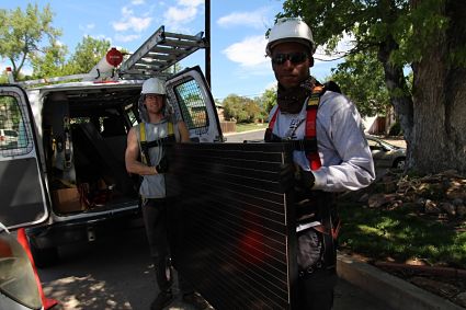 Two workers installing a solar panel on a van in a sunny outdoor setting