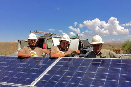 Sergeant Alvin Harvey, Steven Bitah & John Bitah smile behind a solar panel